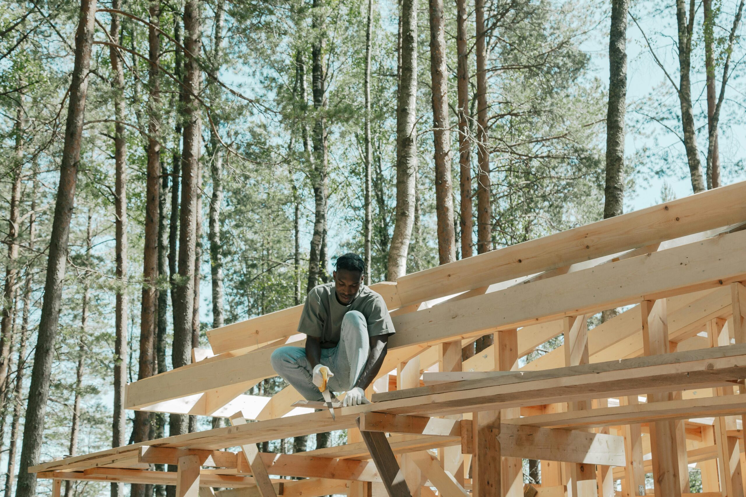 An adult man working on a wooden construction project in a sunny forest setting.